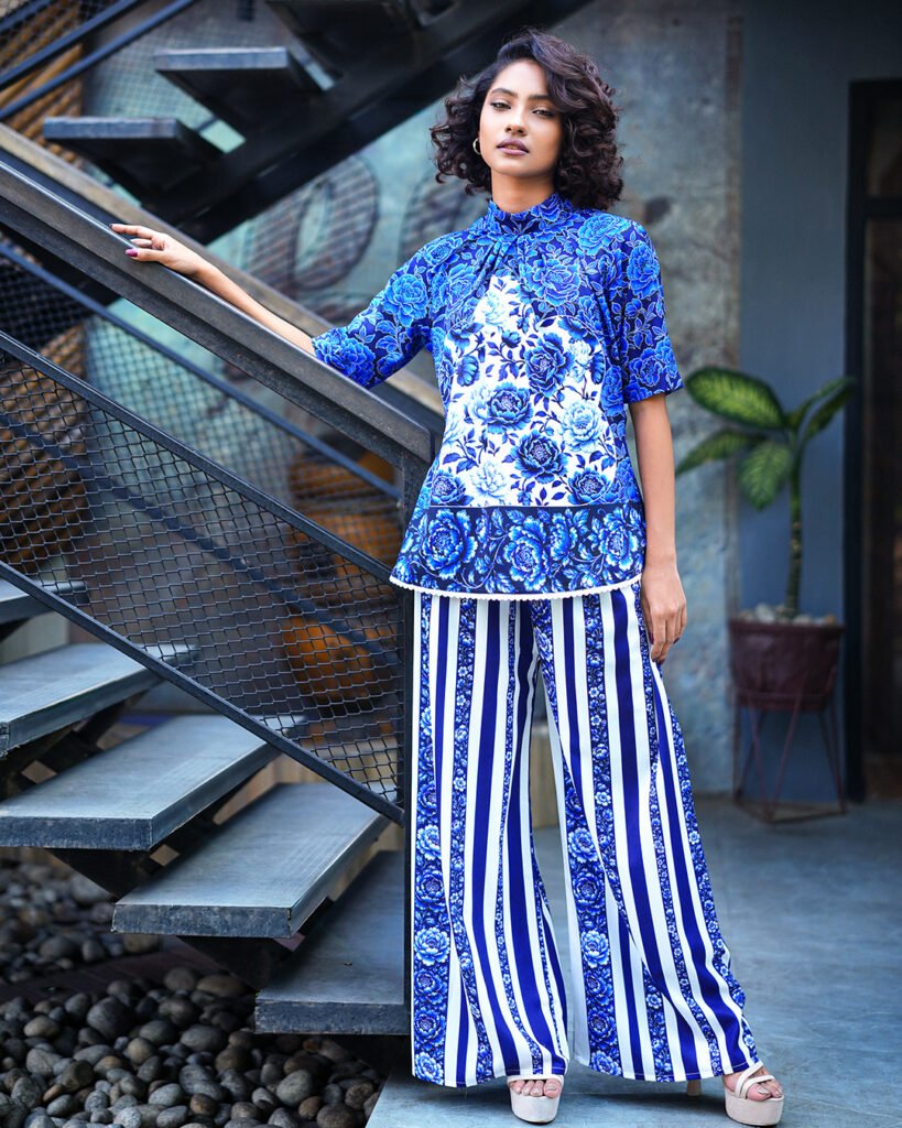 Model wearing ARIZA Blue Floral Co-ord Set with a tie-neck top and blue-and-white striped wide-leg trousers.